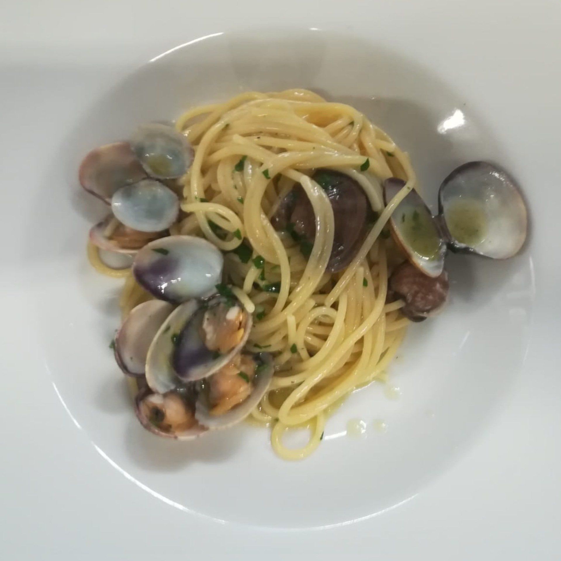 Spaghetti alle vongole in una ciotola bianca. Le vongole sono aperte e cosparse di prezzemolo.