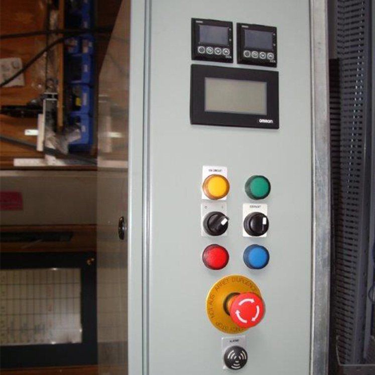 Panneau de commande avec boutons, écrans d'affichage et bouton d'arrêt d'urgence.