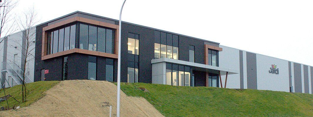 Bâtiment commercial moderne avec des boiseries sombres, de grandes fenêtres et une colline herbeuse en façade.