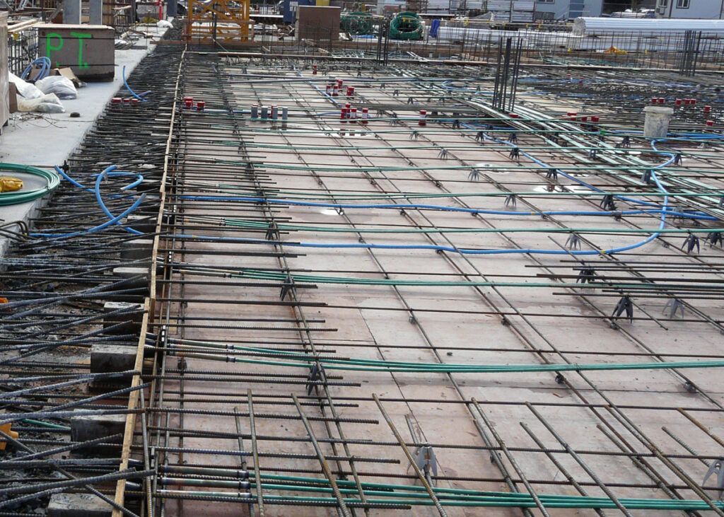 Construction site: reinforced concrete slab with rebar grid, blue pipes, and scaffolding.