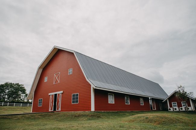 Red barn with white trim and gray roof on a grassy field under a cloudy sky.