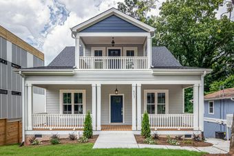 Cottage-style house with two-story porch in gray and navy blue. Lush green lawn and bright blue sky.