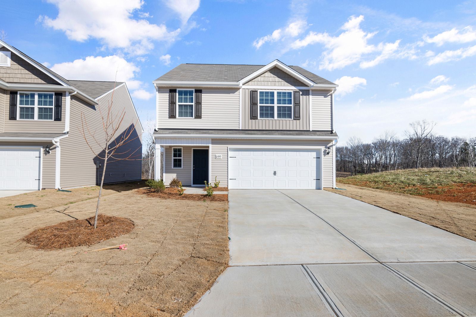 Two-story beige house with a gray roof, black shutters, and a two-car garage on a sunny day.