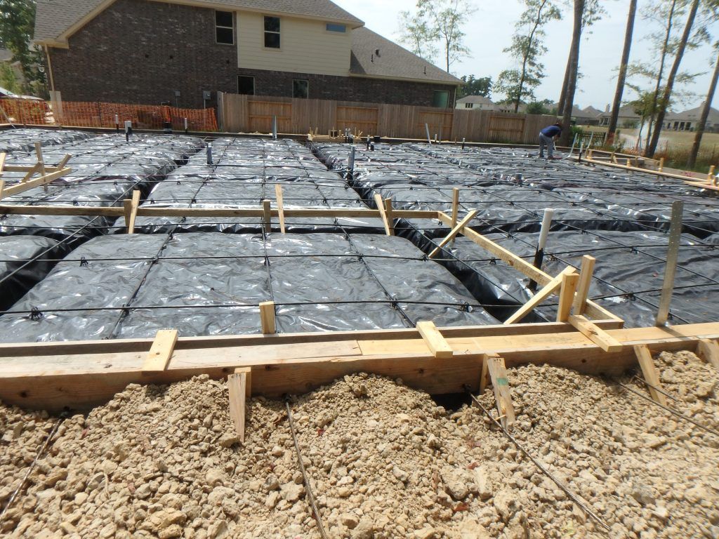 Foundation construction site with wooden forms, black plastic sheeting, and dirt.
