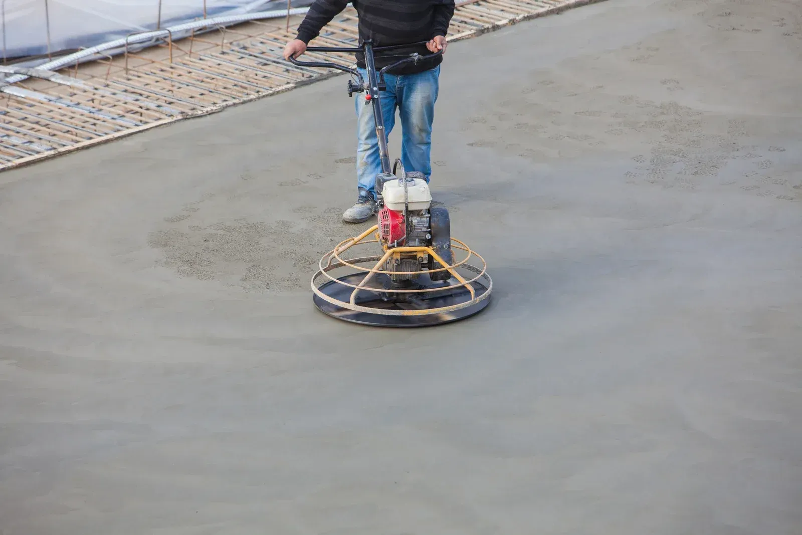 Man using a power trowel to smooth wet concrete.