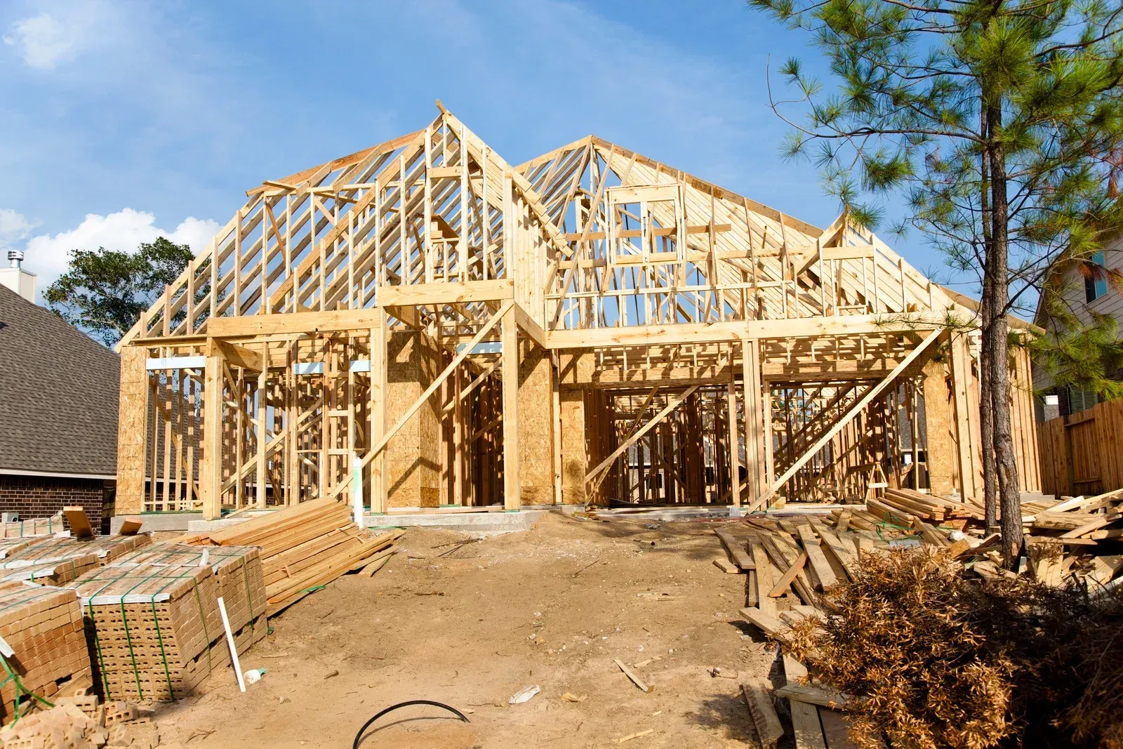 Construction framing of a house under a blue sky. Wooden beams form walls, roof, and openings for windows.