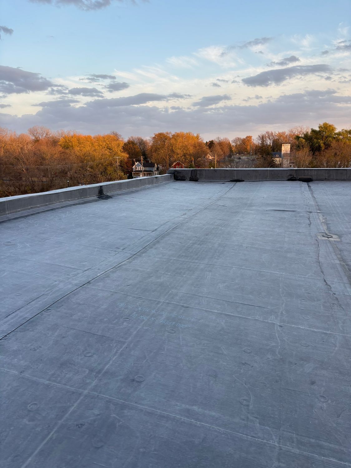 A roof with trees in the background and a blue sky with clouds.