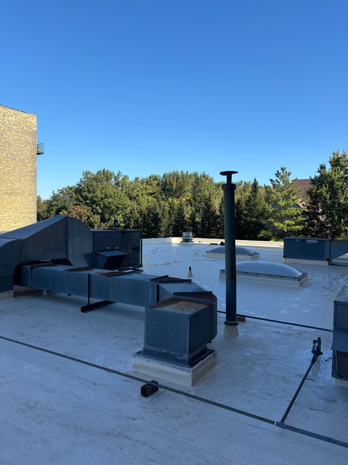 A rooftop with a lot of pipes on it and trees in the background.