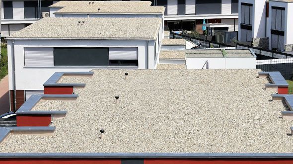 The roof of a building with a gravel roof and a row of houses in the background.