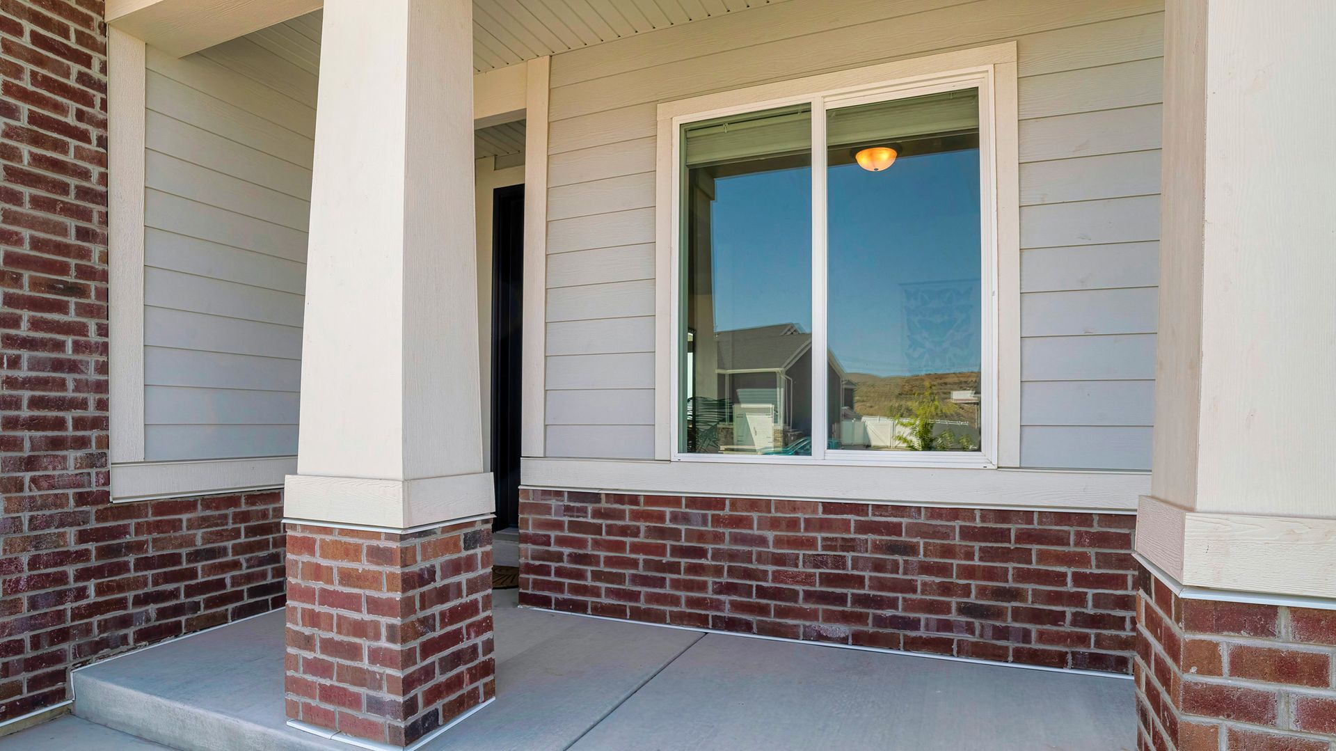 The front porch of a house with brick columns and a large window.
