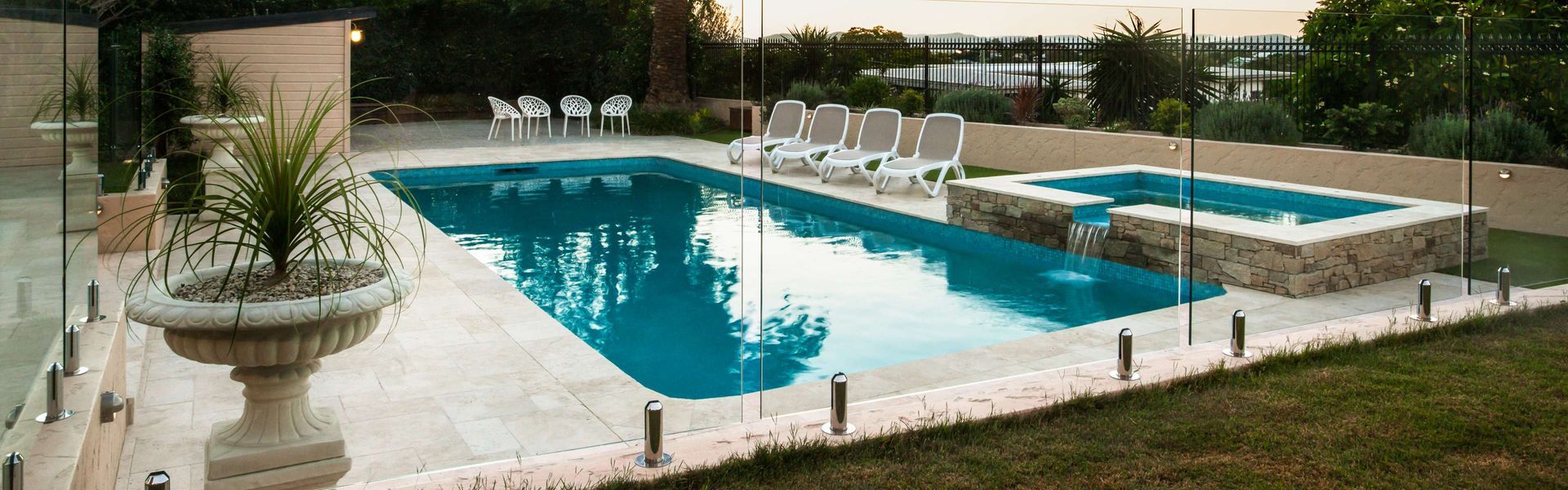 Backyard swimming pool with turquoise water, white lounge chairs, and a potted plant by a stone patio — KLS Fencing In Tablelands, QLD