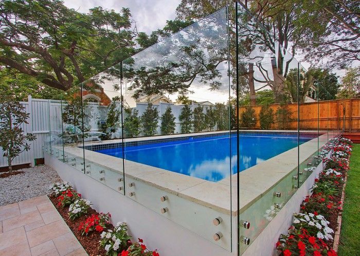 Modern backyard pool with glass railing, surrounded by trees and red flowers — KLS Fencing In Edmonton, QLD