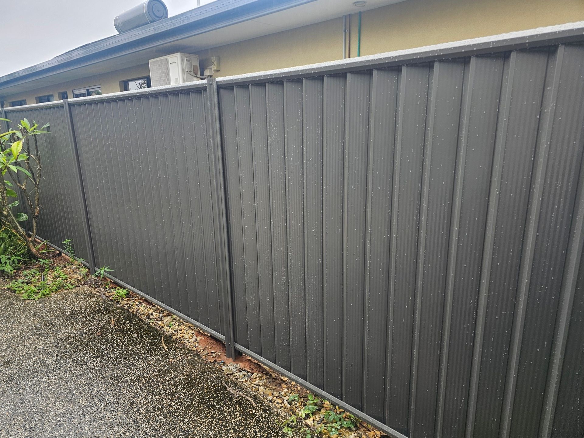 Dark gray metal fence along a gravel driveway beside a house — KLS Fencing In Normanton, QLD