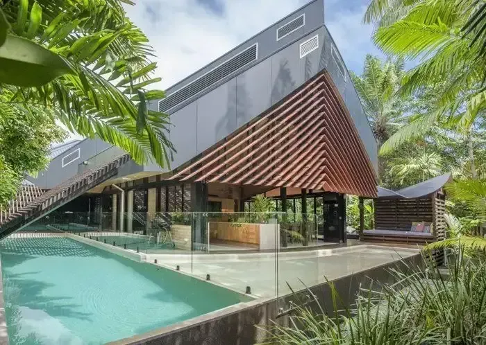 Modern tropical resort with angular gray buildings, wooden slats, and a turquoise pool surrounded by palm trees — KLS Fencing In Normanton, QLD