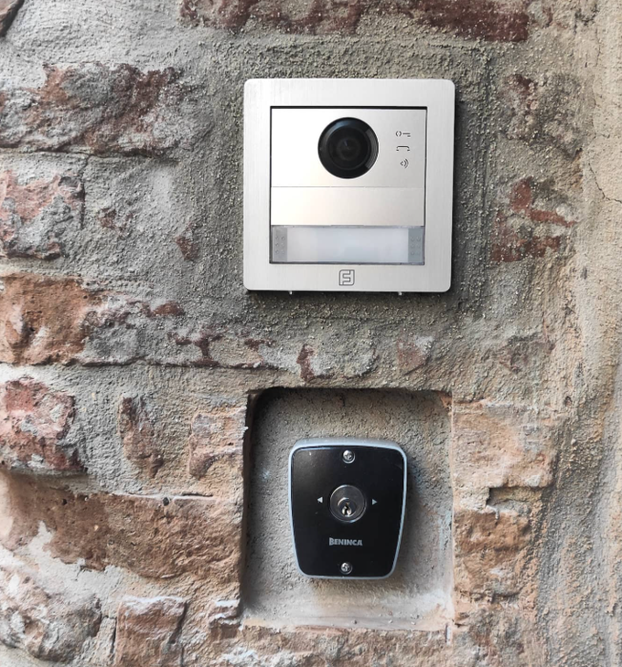 Due campanelli/citofoni con videocamera su un muro di mattoni: un'unità rettangolare argentata sopra un'unità quadrata nera.