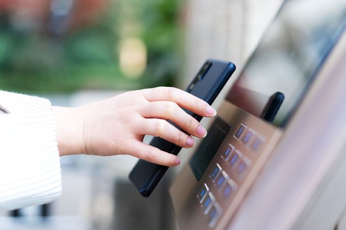 Mano di una persona con un telefono nero che tocca il terminale di pagamento; probabilmente si sta utilizzando un pagamento contactless.
