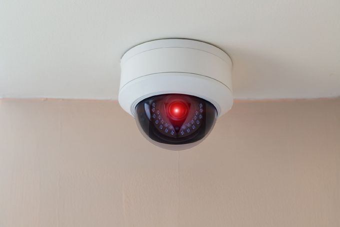 Telecamera di sicurezza montata su un soffitto beige, con una luce rossa che indica l'attività.