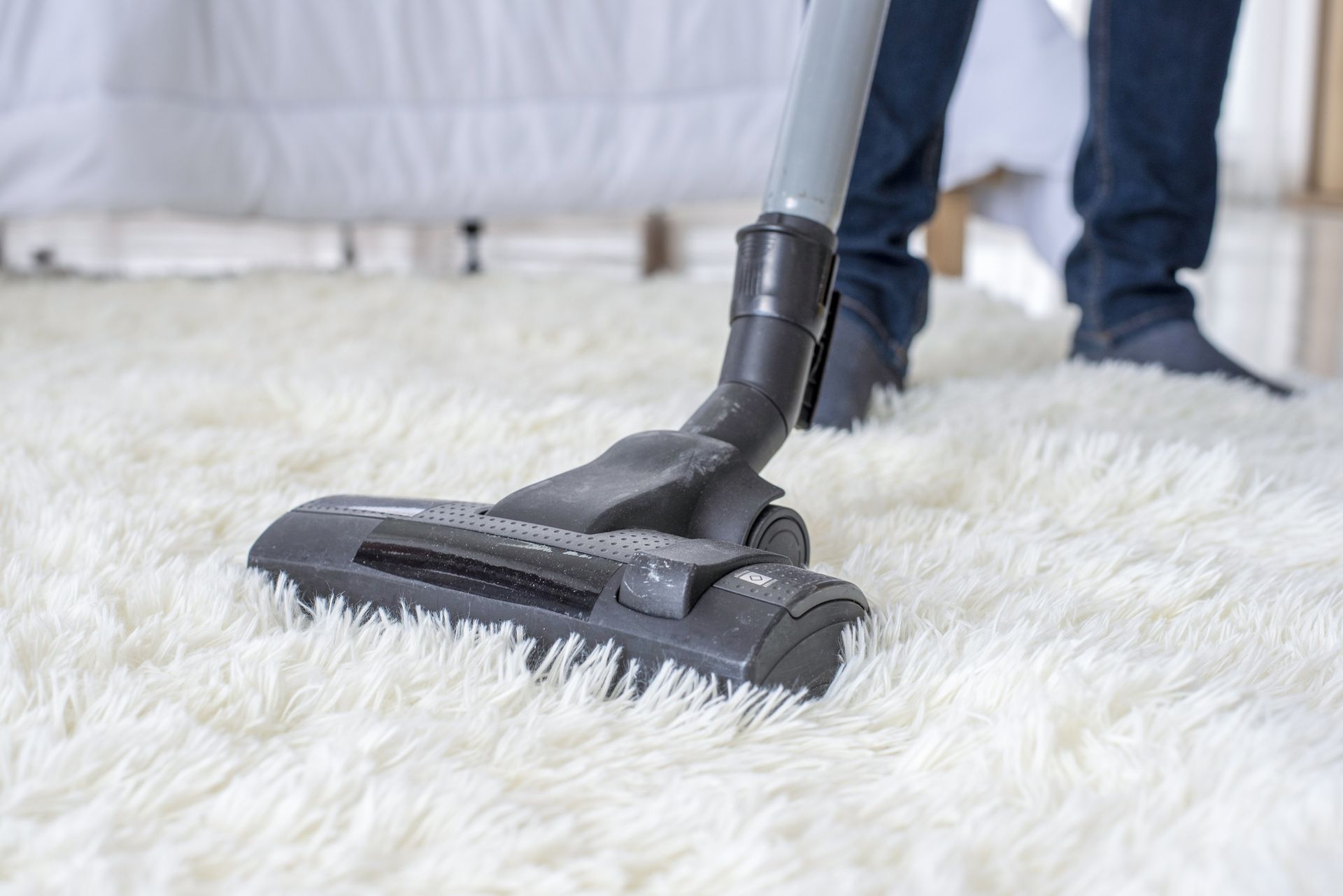 Person vacuuming a white fluffy rug with a vacuum cleaner in a room.