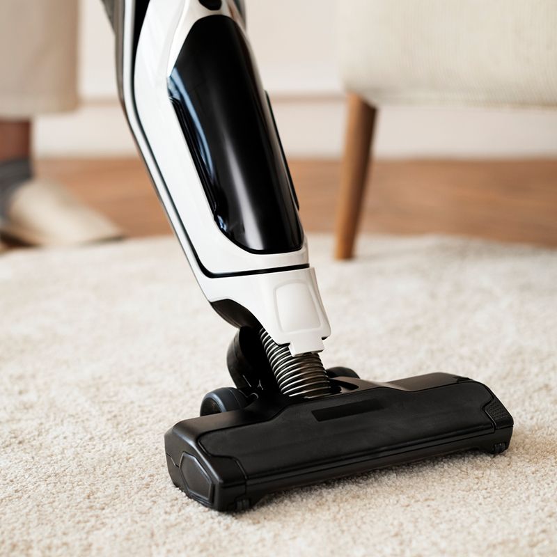 A person vacuuming a white carpet with a black and white cordless vacuum cleaner.