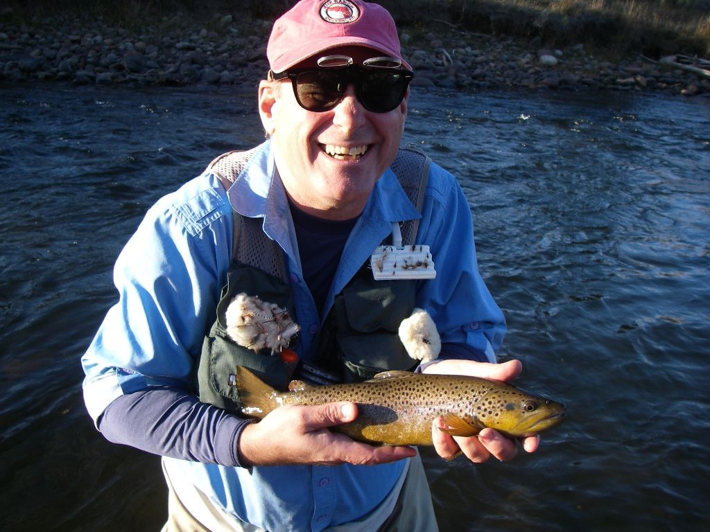 A man in a blue shirt is holding a brown trout