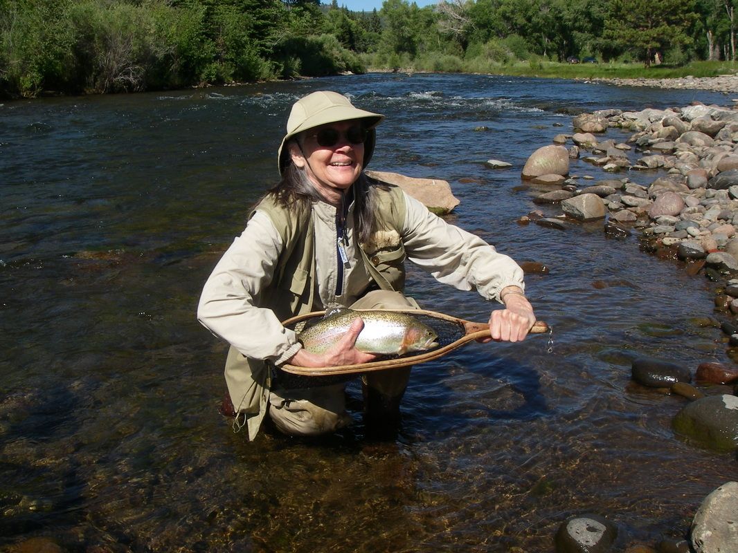 A woman is kneeling in the water holding a fish in a net
