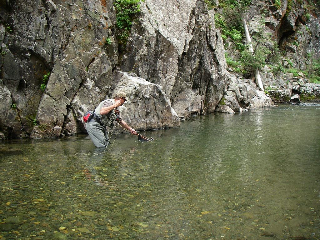 A man is fishing in a river surrounded by rocks.