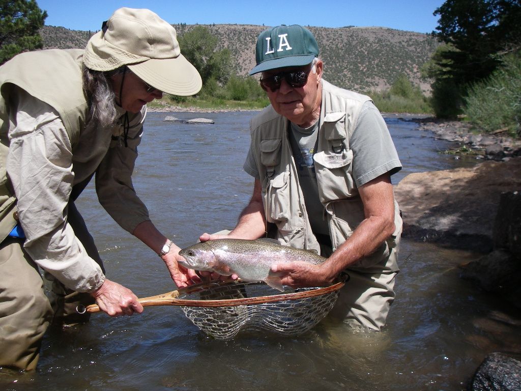 A man wearing a la hat is holding a fish in a net