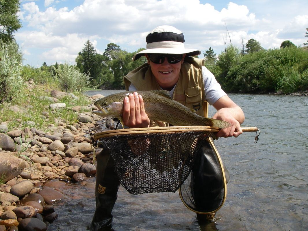 A man is kneeling in the water holding a fish in a net