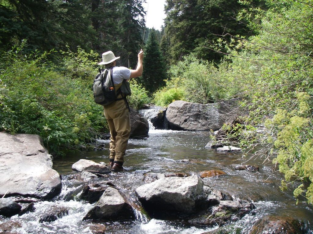 A man in a hat is crossing a river on rocks.