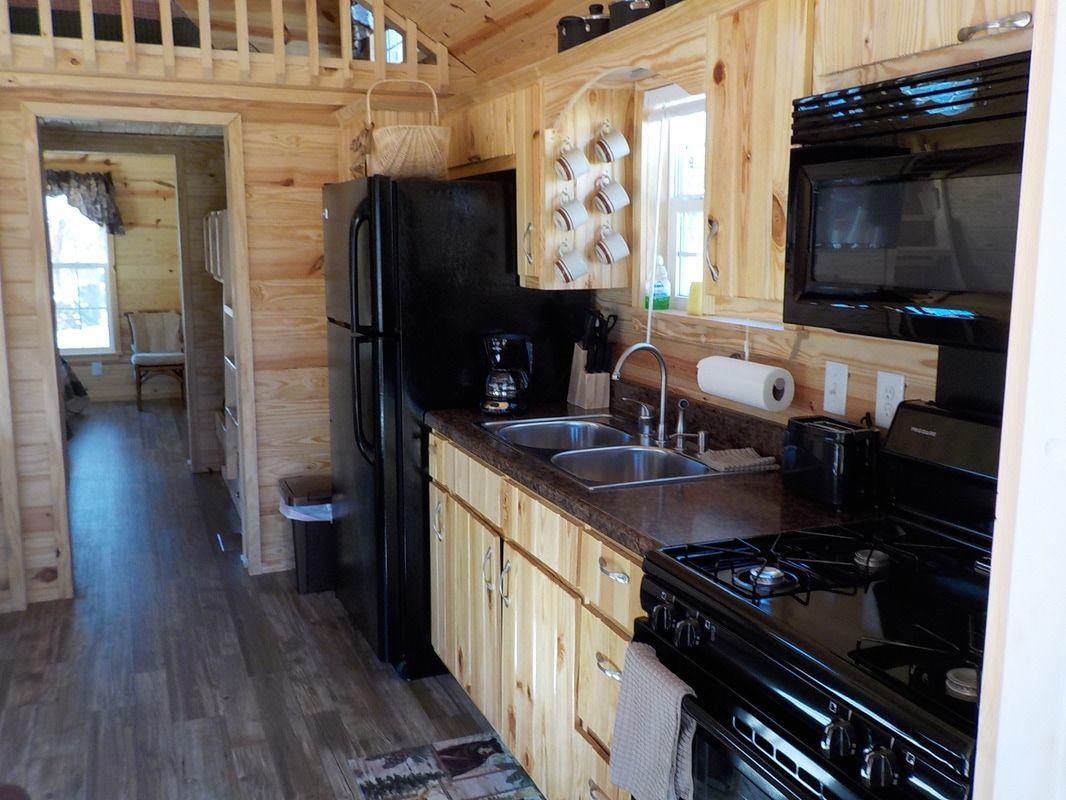 A kitchen in a log cabin with a refrigerator , stove , sink and microwave.
