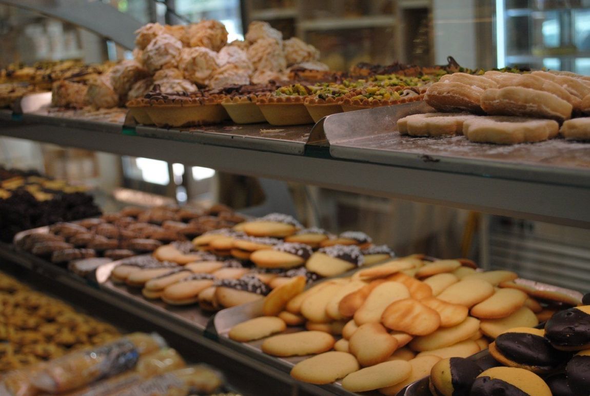 Assortimento di pasticcini e biscotti esposti su vassoi da pasticceria dietro un bancone di vetro.