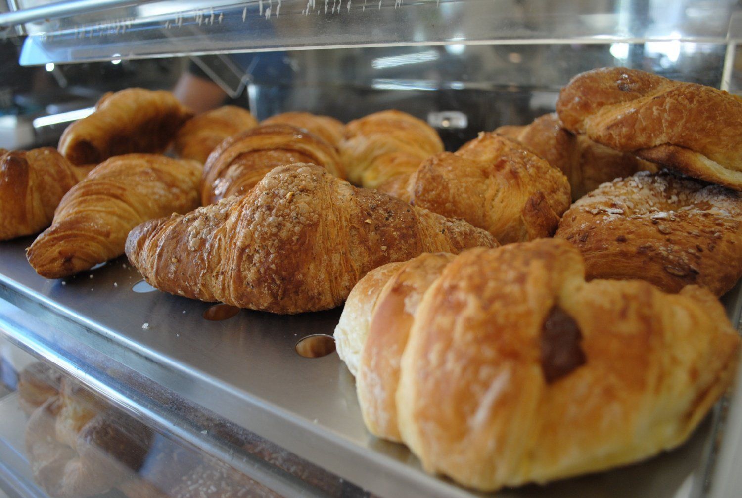 Vassoio di croissant e pasticcini dorati su un bancone espositivo di una pasticceria.