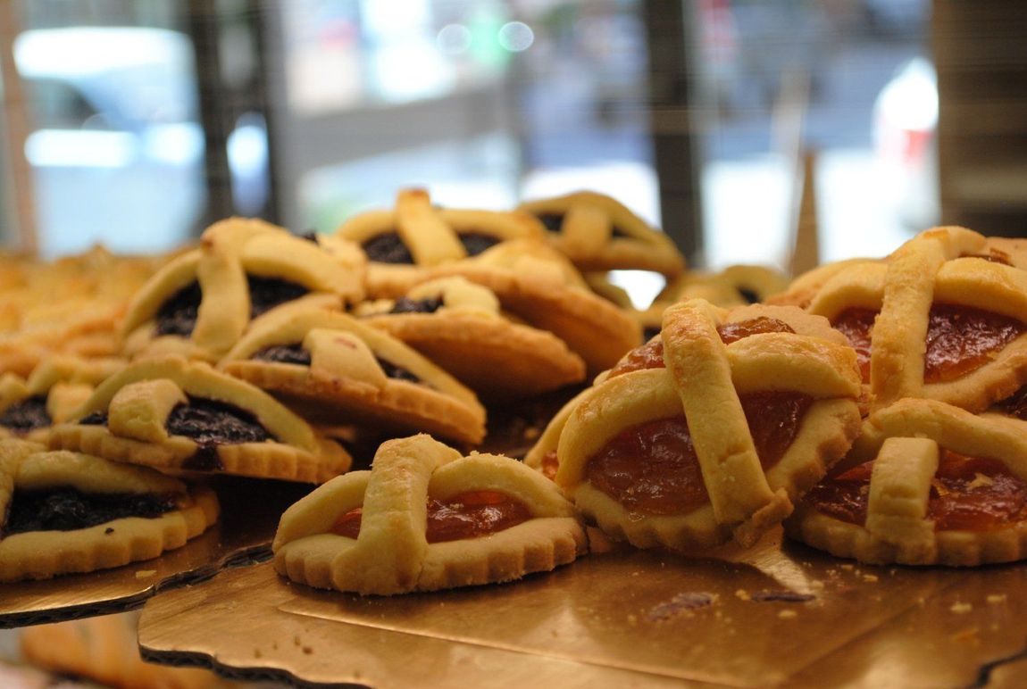 Assortimento di pasticcini e biscotti esposti su vassoi da pasticceria dietro un bancone di vetro.