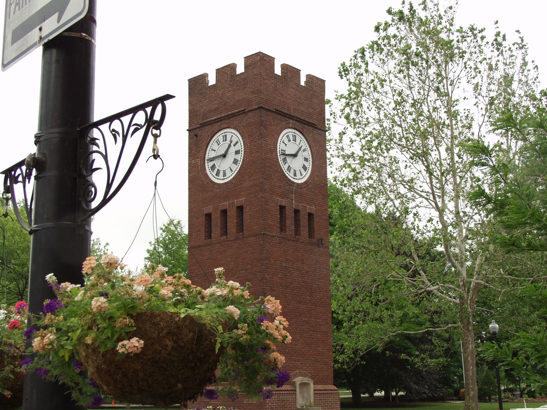 A brick tower with two clocks on it and flowers in front of it