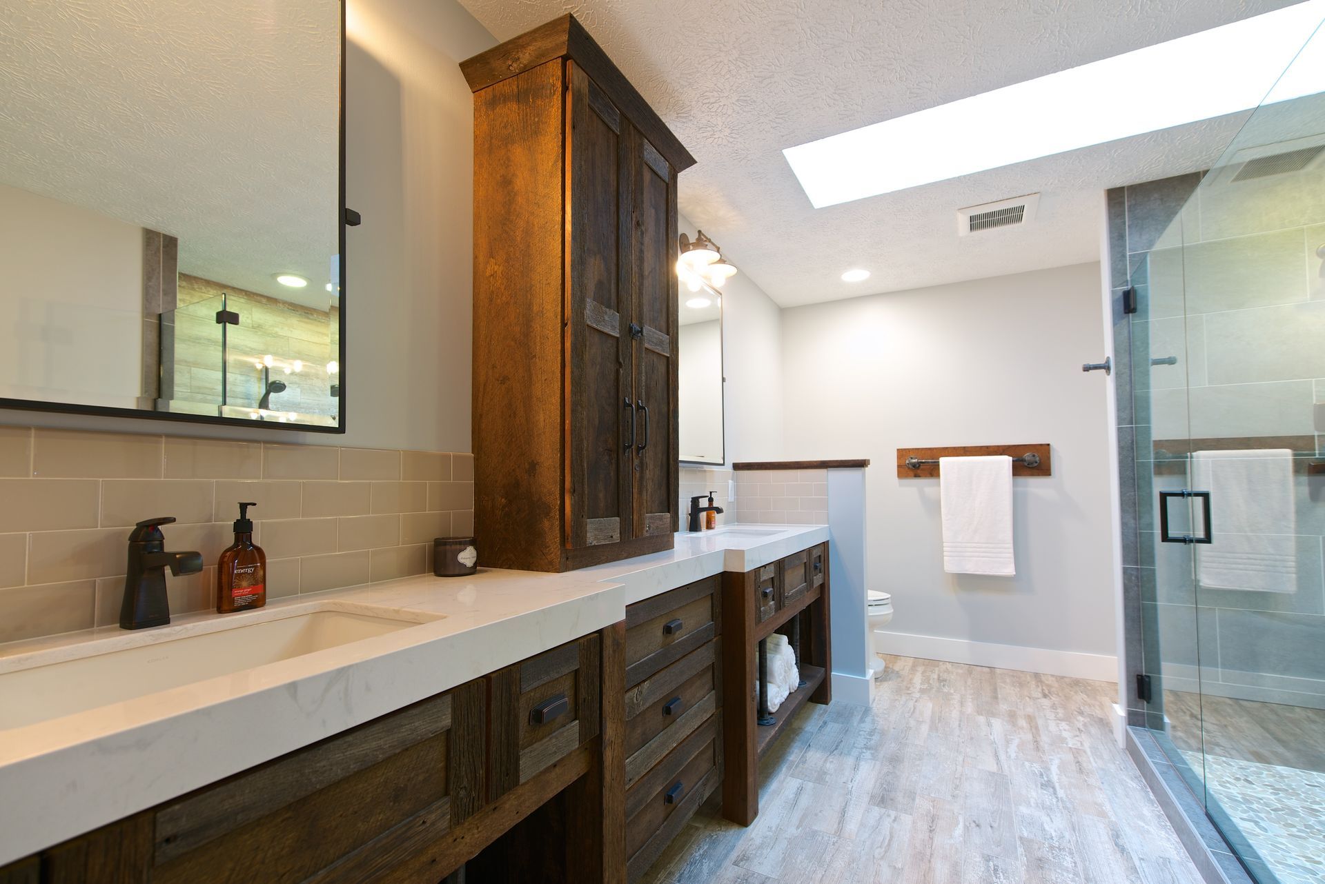 Rustic bathroom with wooden vanity, tall cabinet, stone countertop, and glass shower.