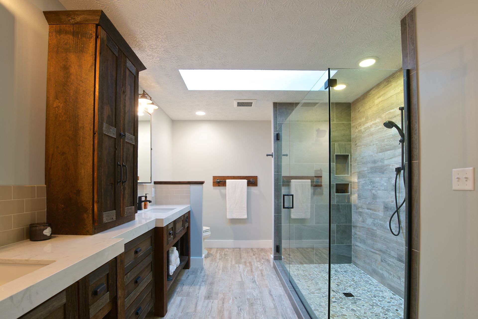 Rustic bathroom with wood vanity, large shower, and a skylight.