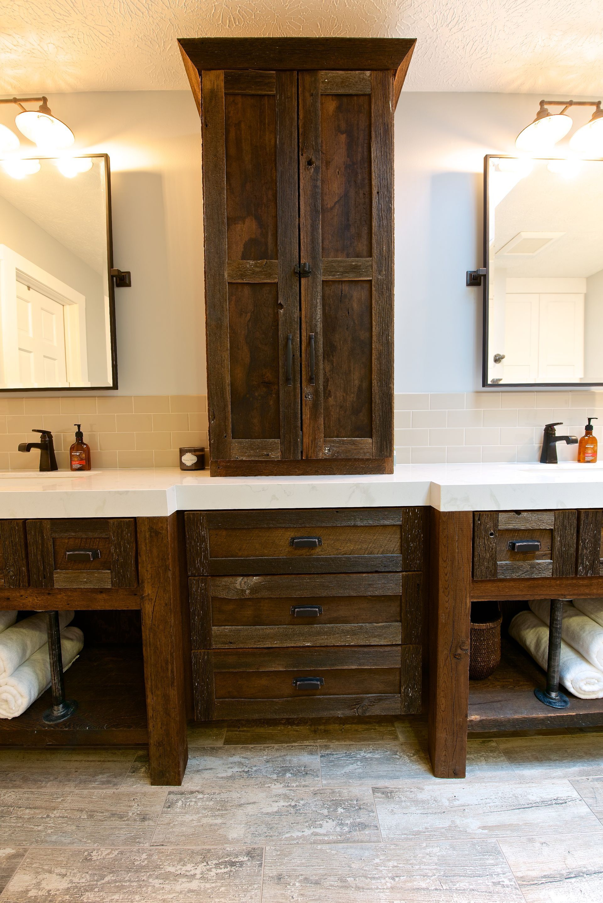 Rustic bathroom with wood vanities, center cabinet, two mirrors, and overhead lighting.