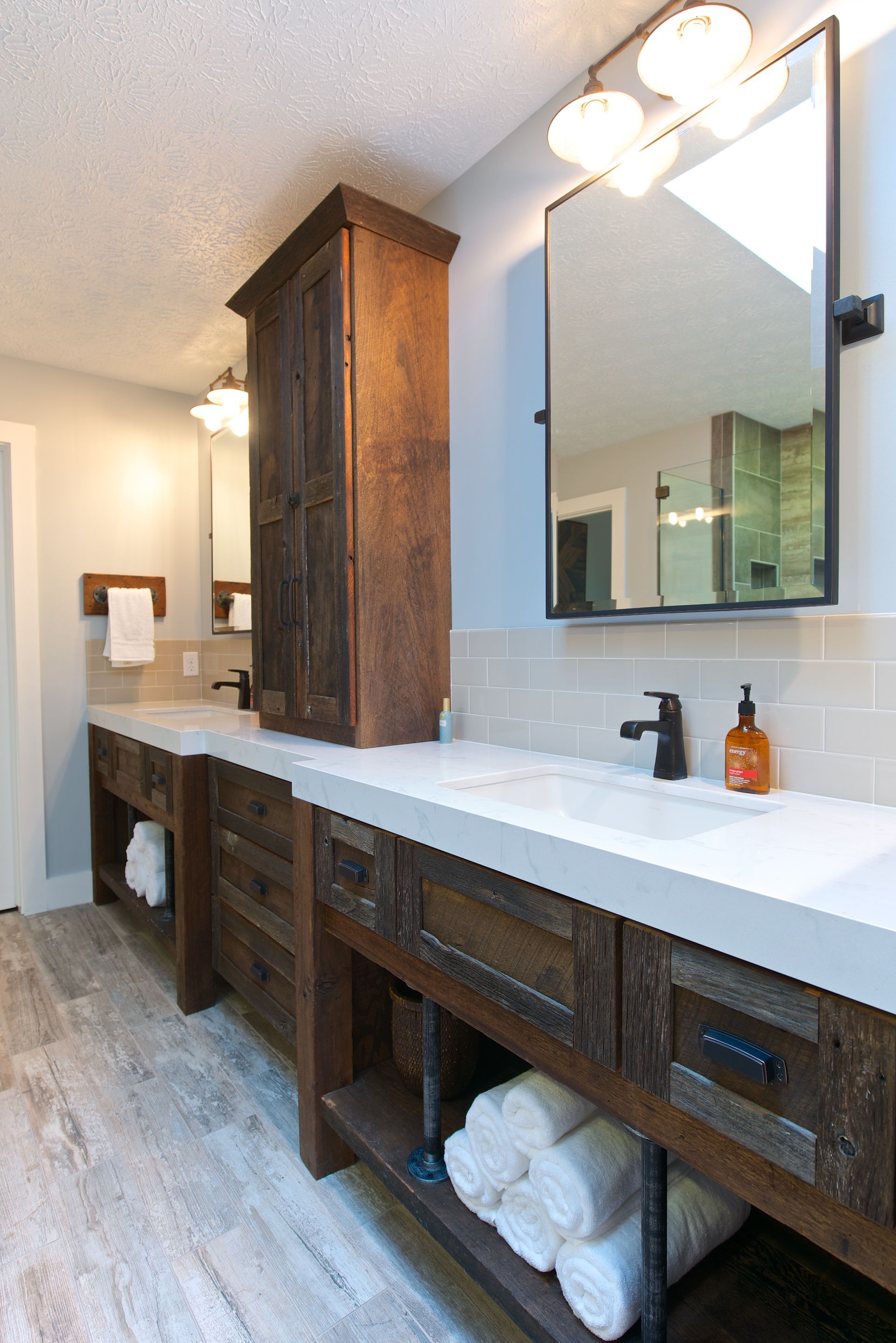 Rustic bathroom with wooden vanities, concrete countertops, and a tall cabinet.