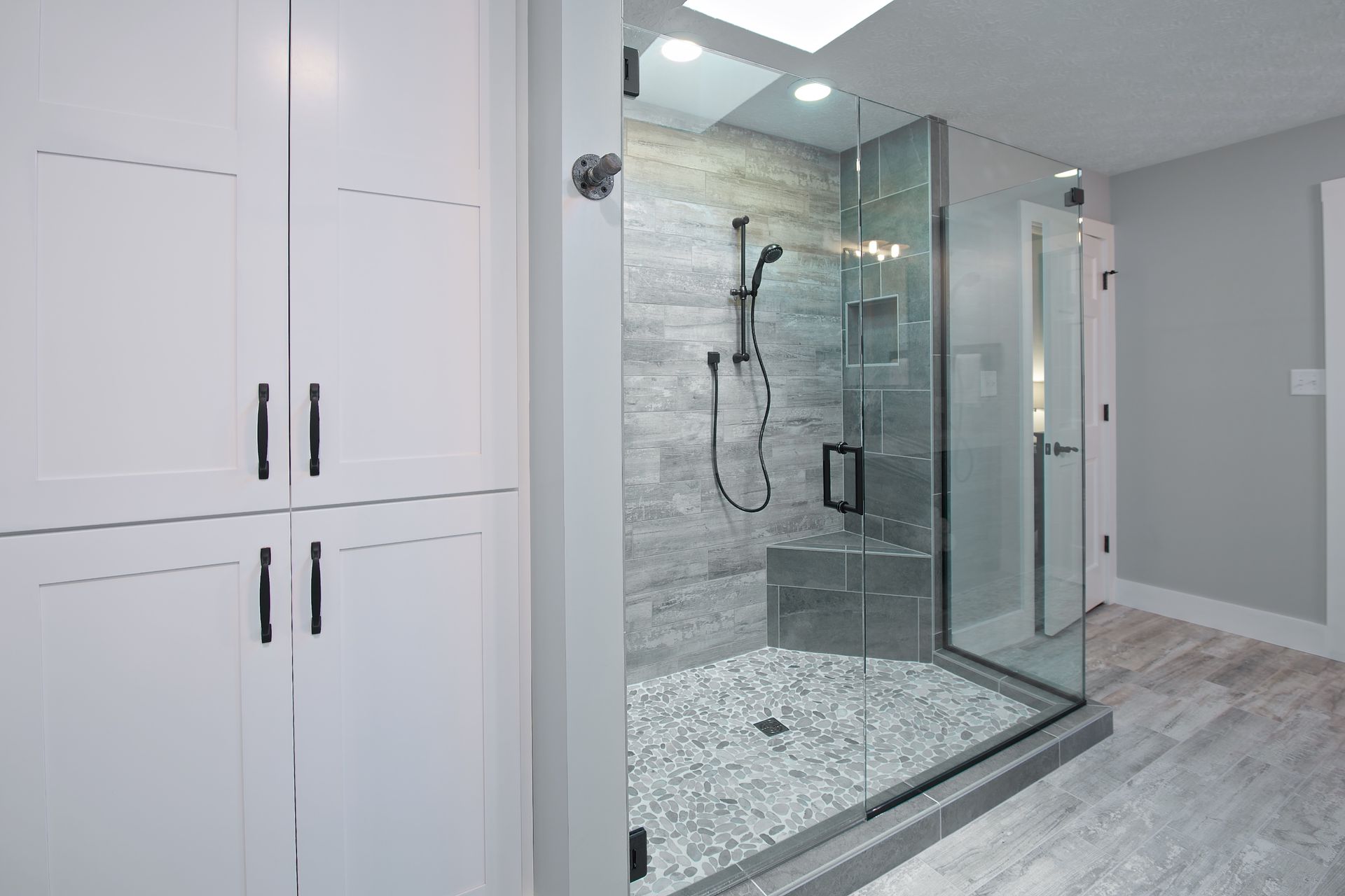 Modern bathroom with glass shower, pebble floor, built-in bench, and white cabinets.