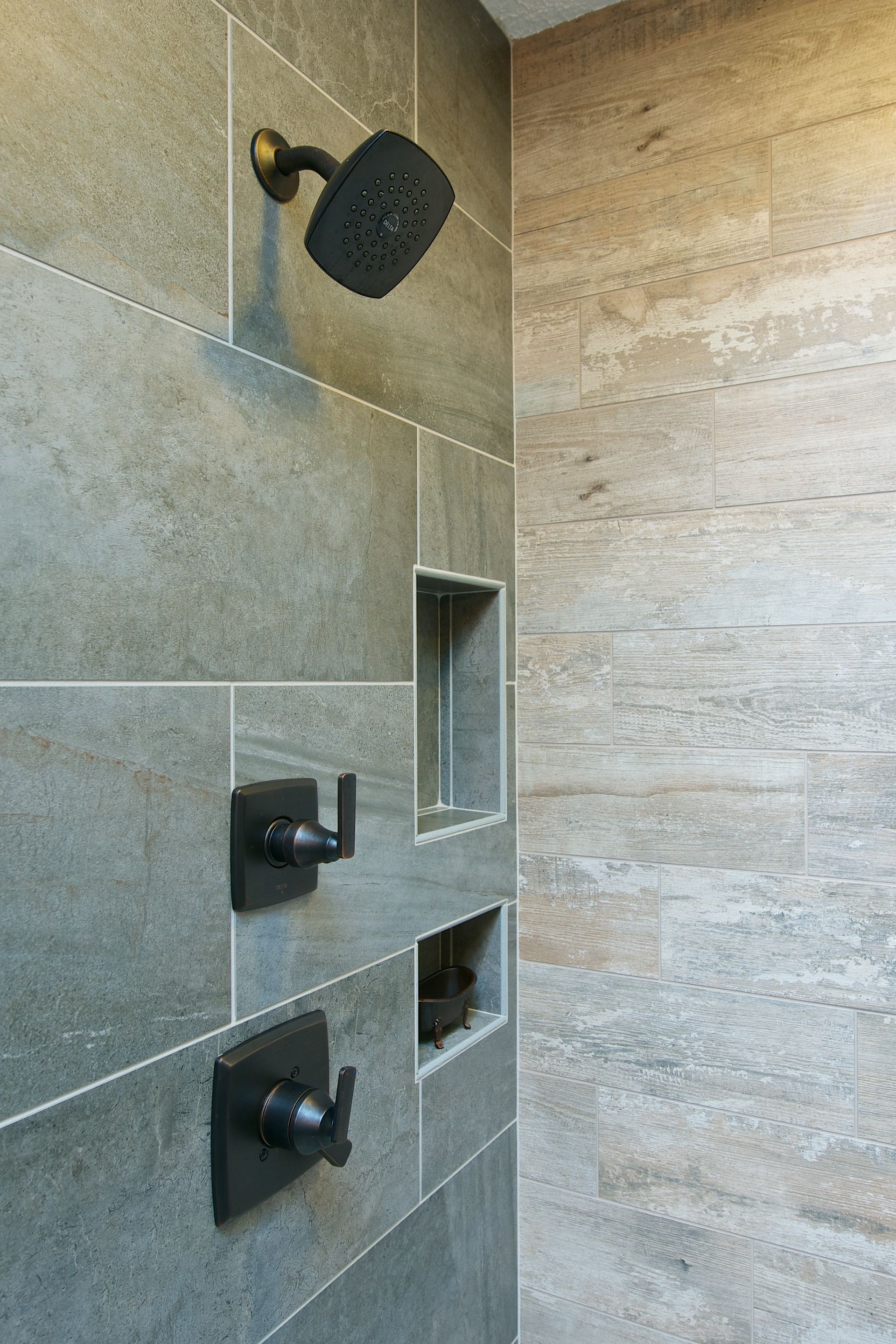 Shower with gray tile, black fixtures, and recessed storage.
