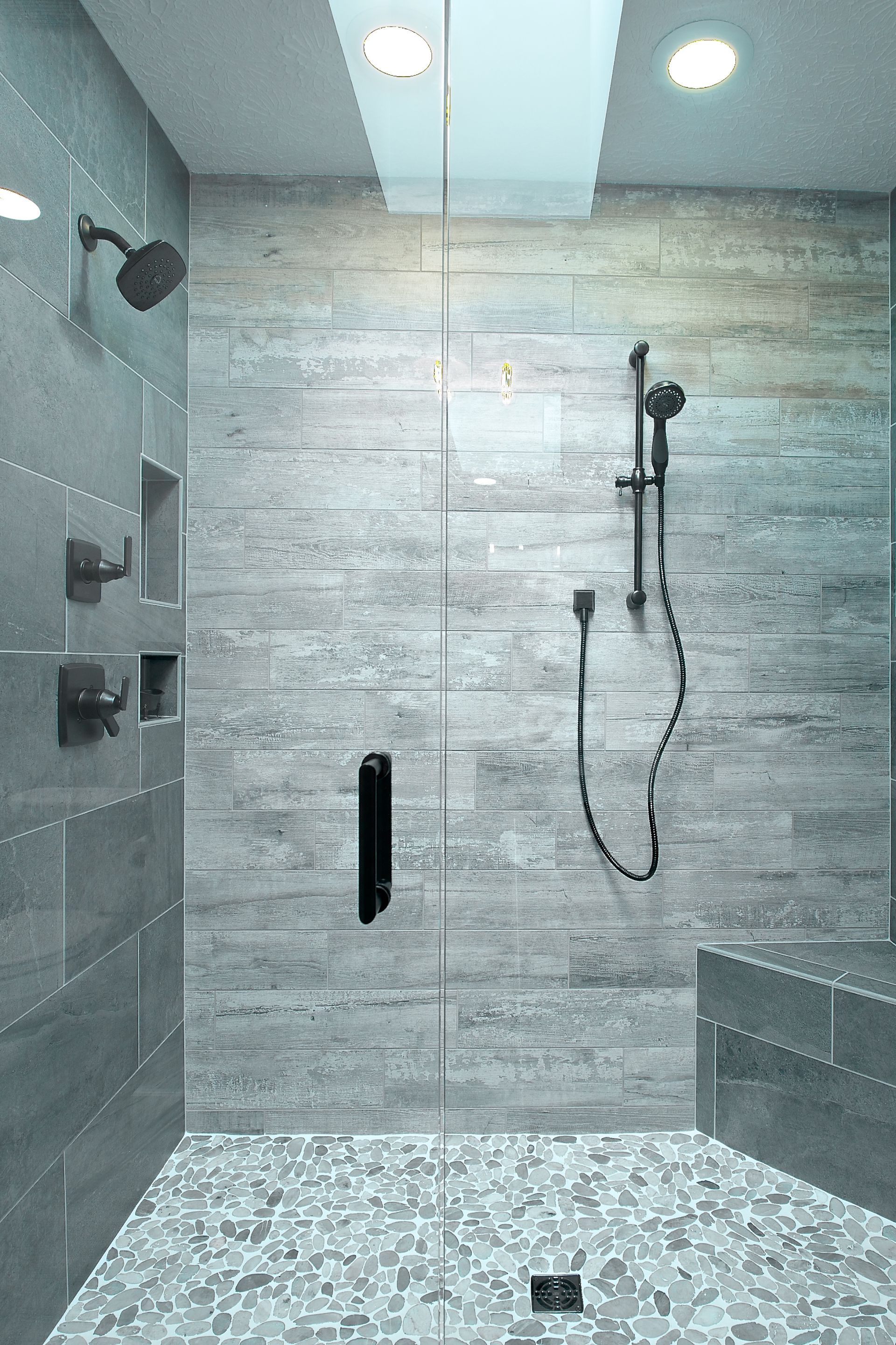 Gray tiled shower with pebble floor, rain shower head, and a sliding glass door.