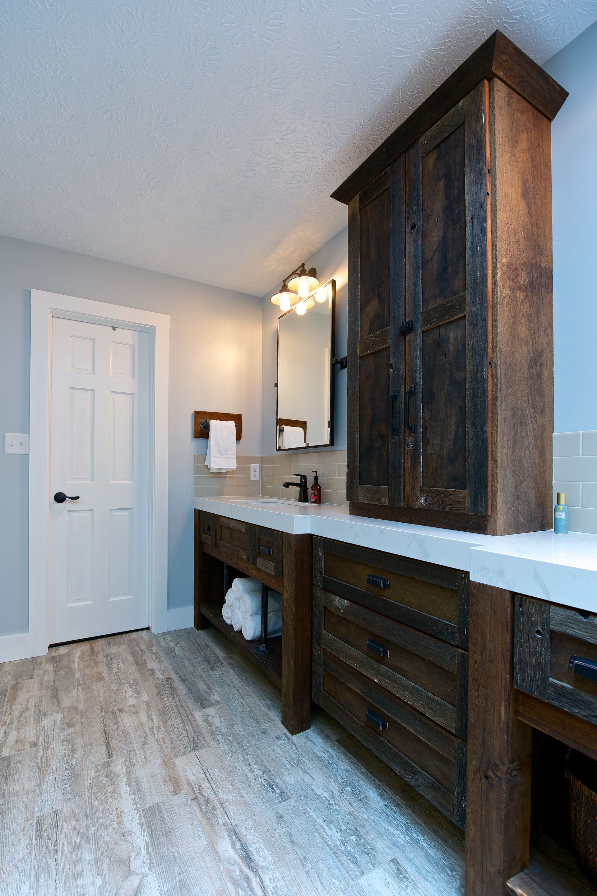 Rustic bathroom with wooden cabinets, white countertop, and gray walls; light wood-look flooring.
