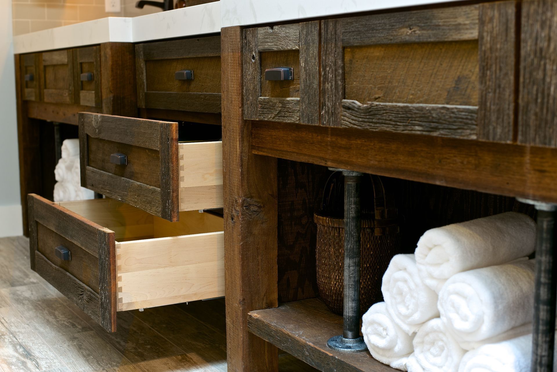 Rustic wooden bathroom vanity with open drawers, towels, and shelving.