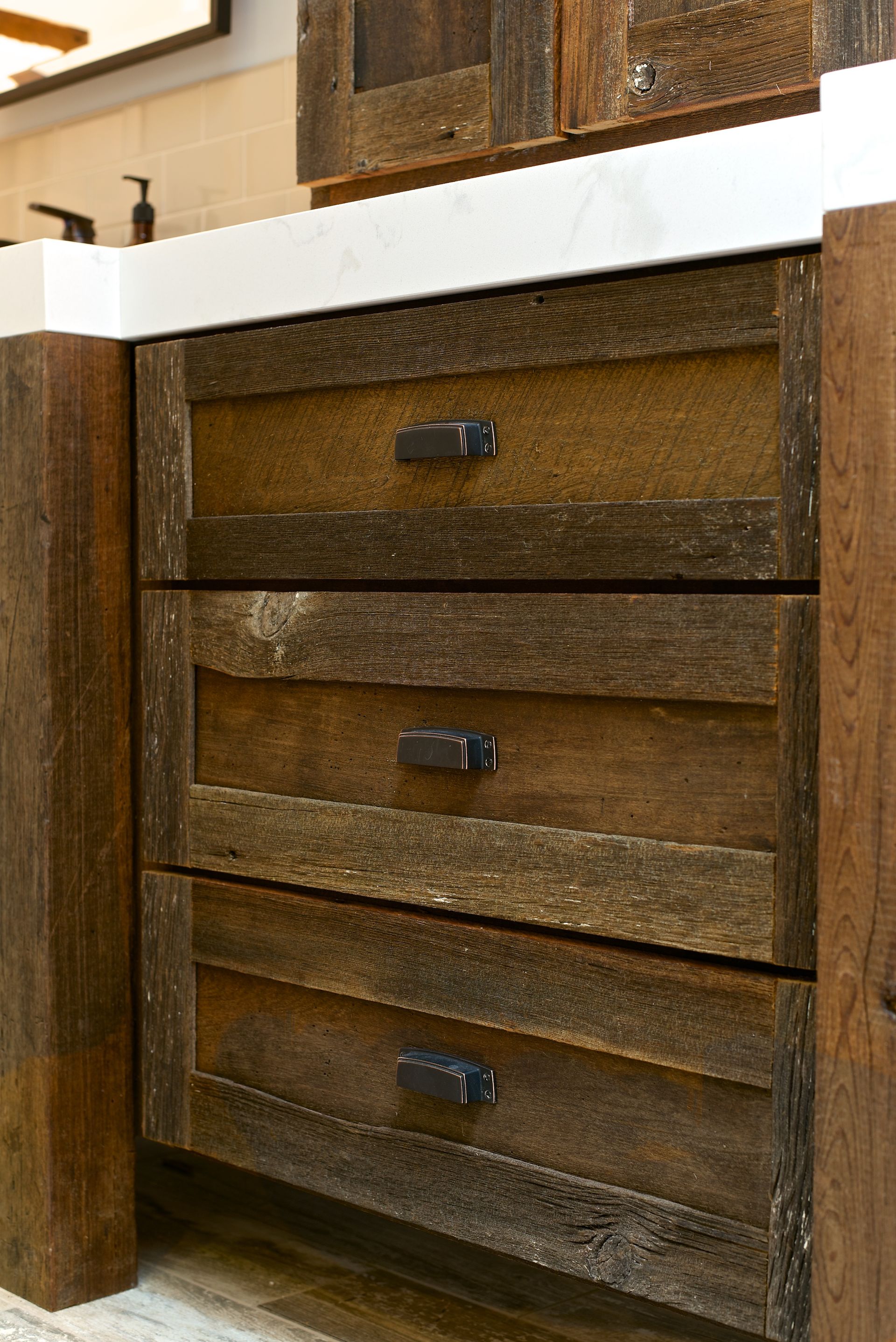 Rustic wooden bathroom vanity with three drawers, marble countertop, and black hardware.