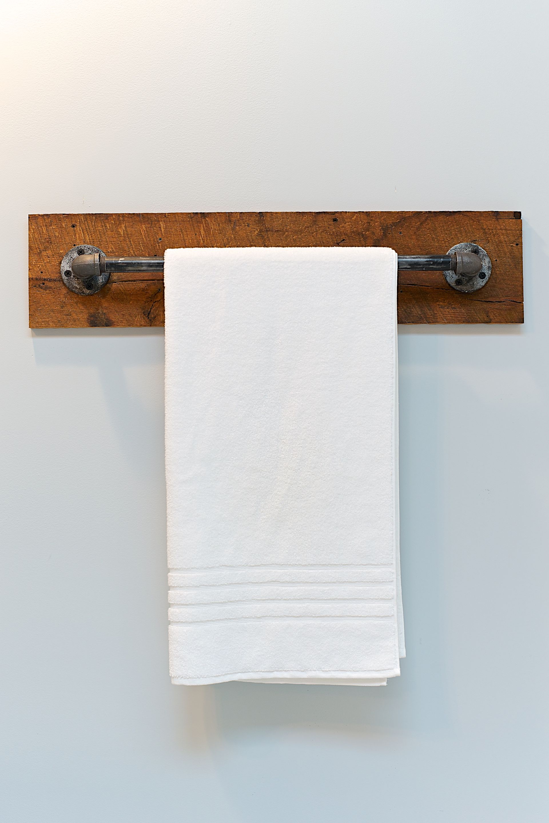 White towel hanging on a rustic towel rack made of wood and metal, mounted on a light blue wall.