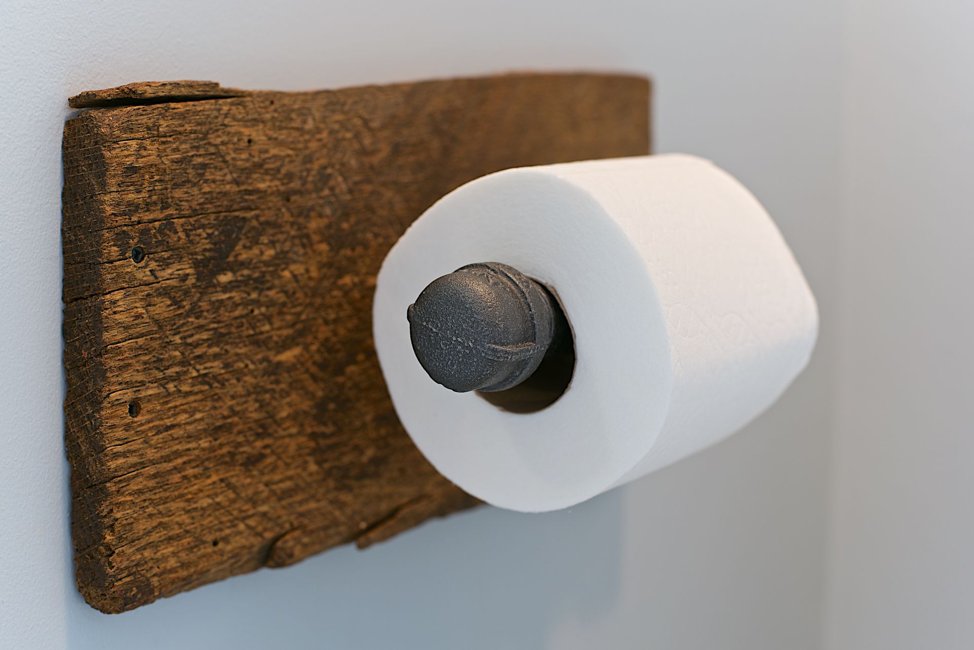 Rustic wooden toilet paper holder with a roll of white toilet paper.
