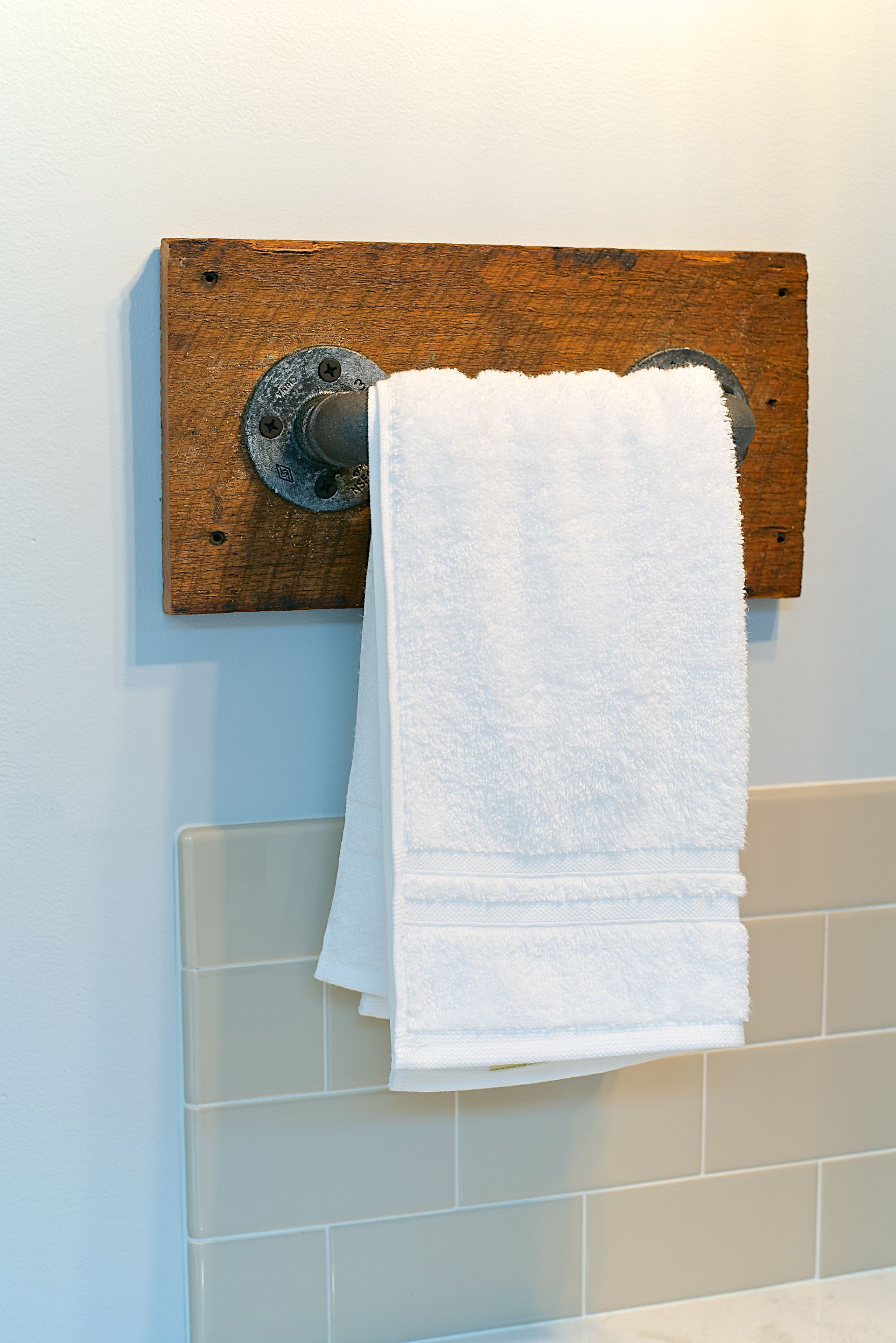 White towel hanging on a rustic, wooden towel rack attached to a wall.