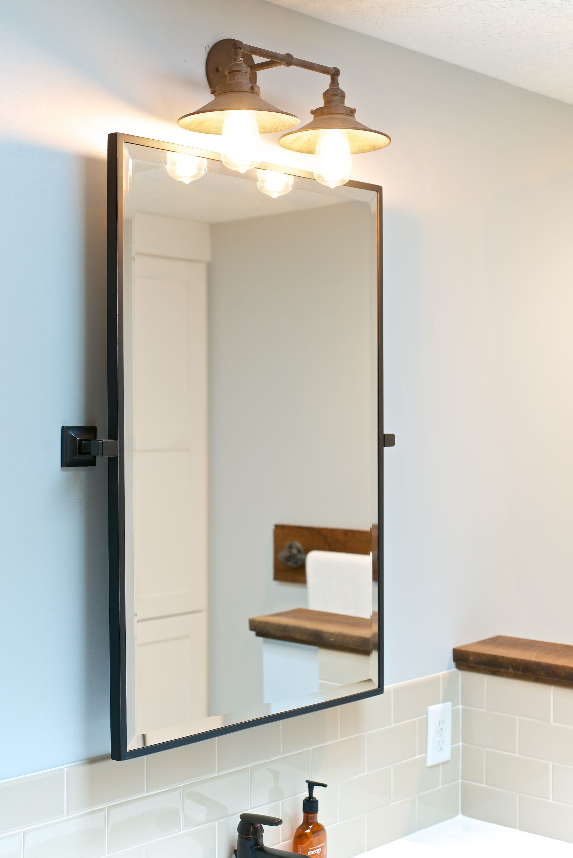 Bathroom mirror with industrial style lighting, reflection of toilet, light blue wall.