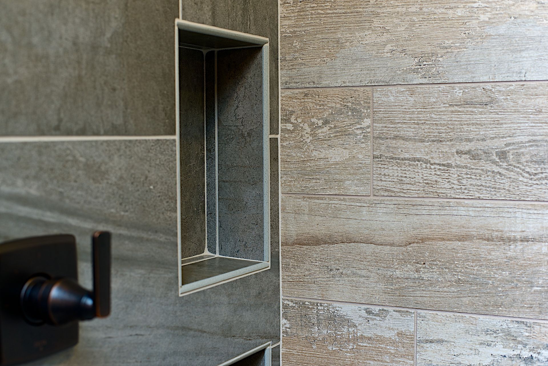 Shower niche built into tiled wall, with a bronze faucet and wooden planks.