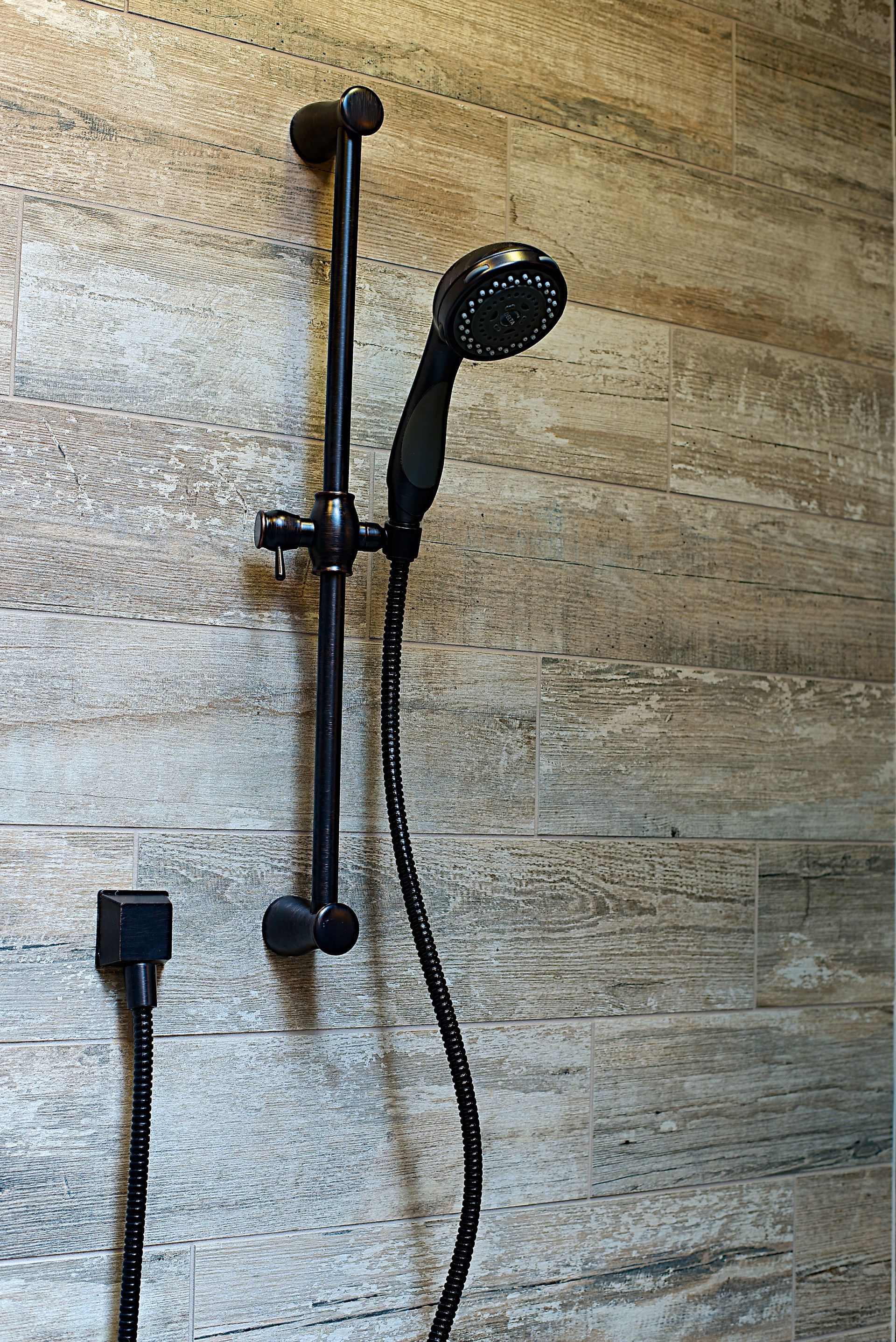 Black showerhead on a vertical bar against a textured, light brown wall.